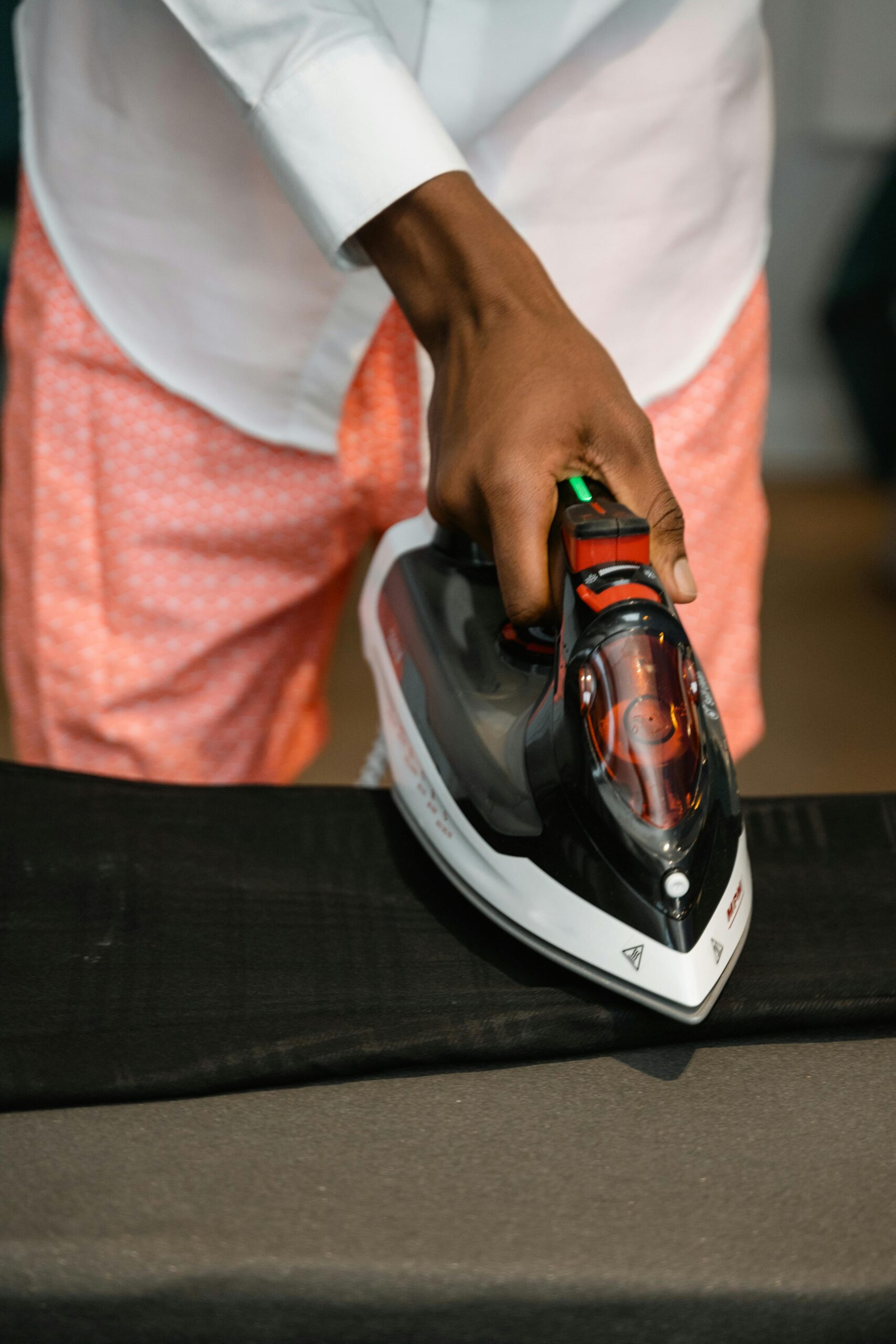 A person ironing black pants indoors, focusing on the task with a modern electric iron.