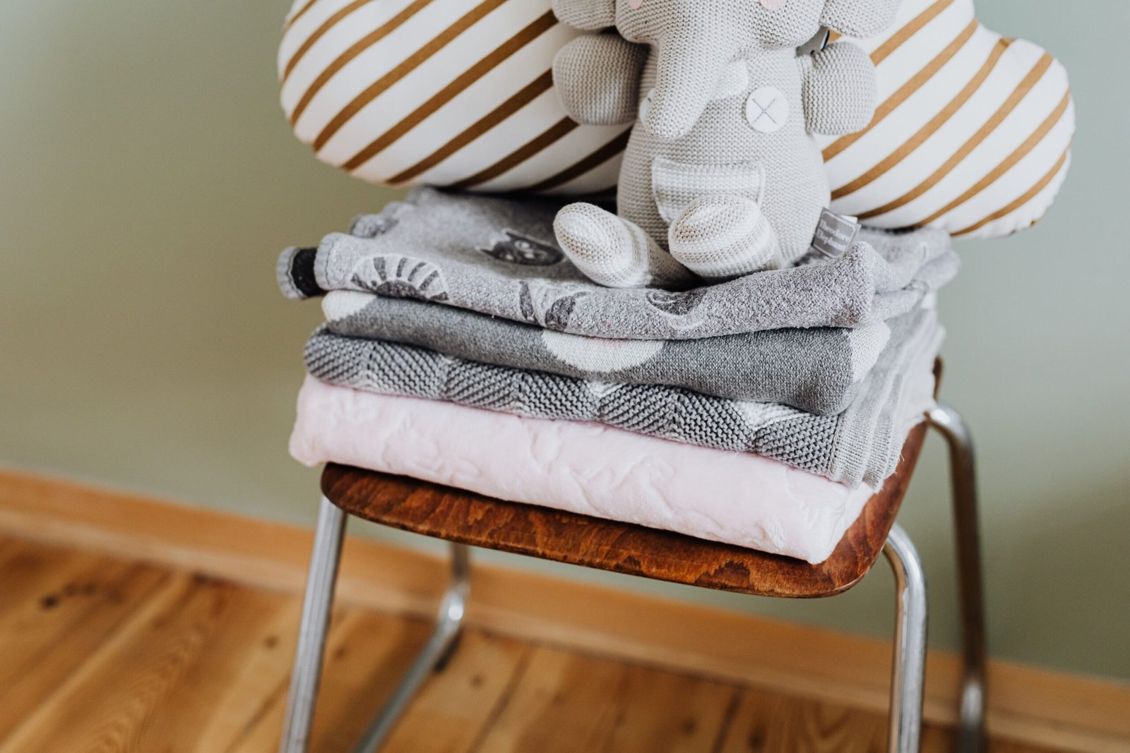 Stack of soft blankets and a plush toy elephant on a wooden chair, exuding warmth and coziness.